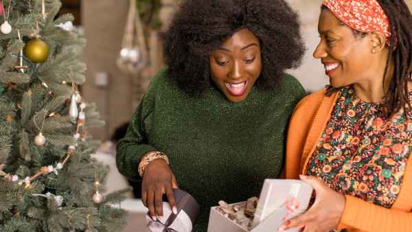 Mother surprising daughter with gift next to Christmas tree