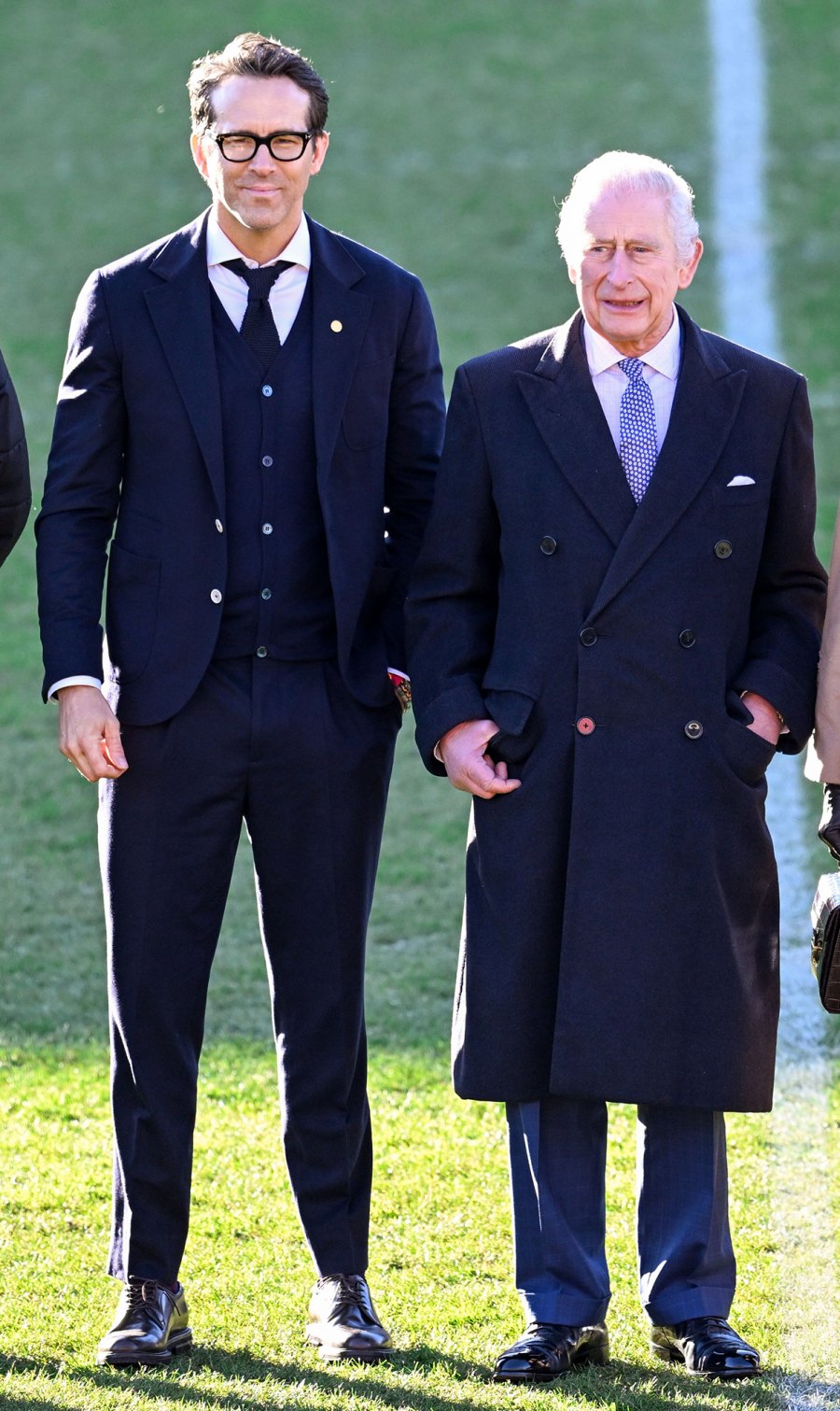 Smiling Ryan Reynolds in a Black Suit next to King Charles III in a coat on a soccer field Hotness Evolution