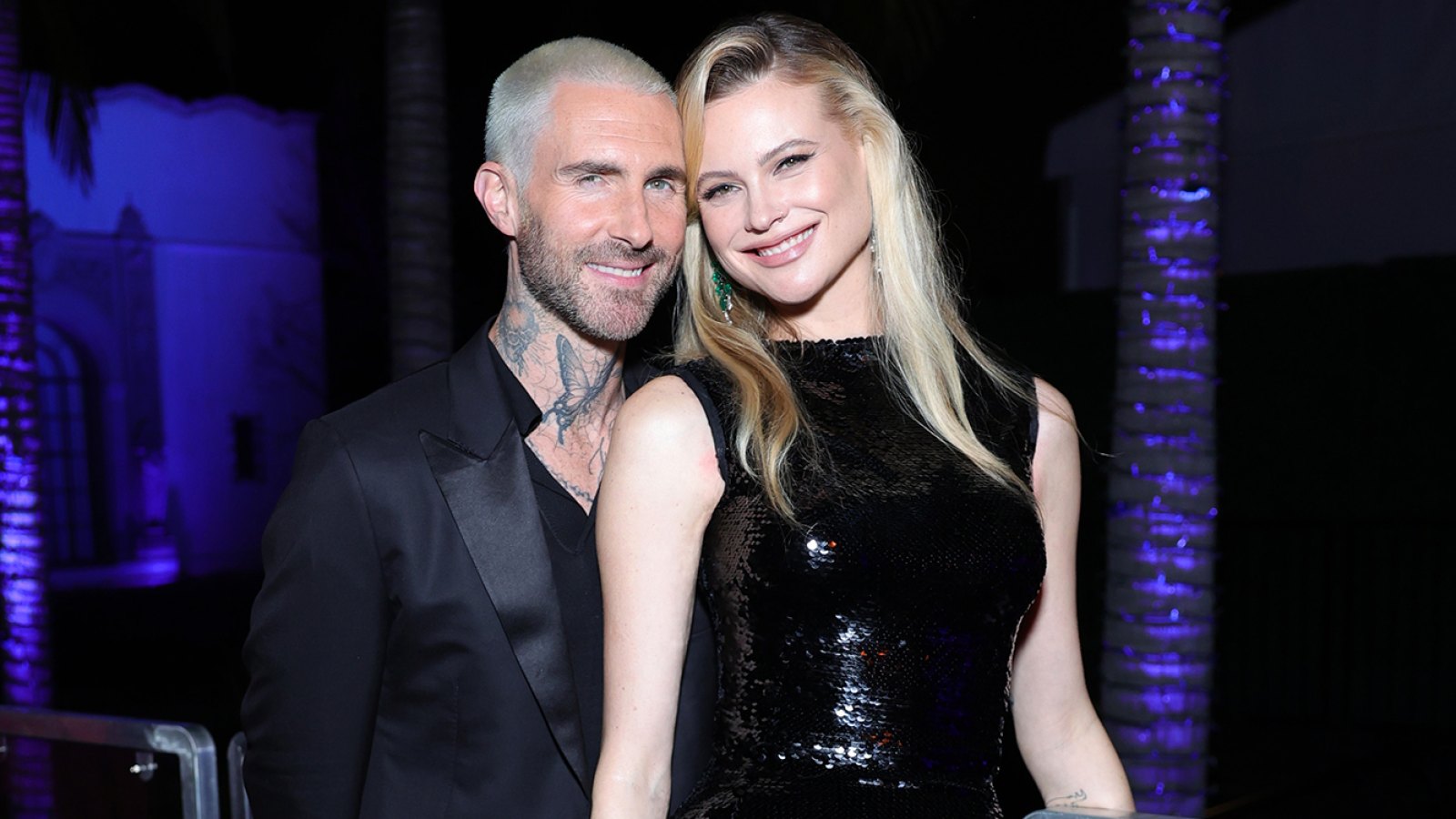 Adam Levine wears a black suit with Behati Prinsloo wearing a black sequin dress as they smile and pose at the Vanity Fair Oscar Party