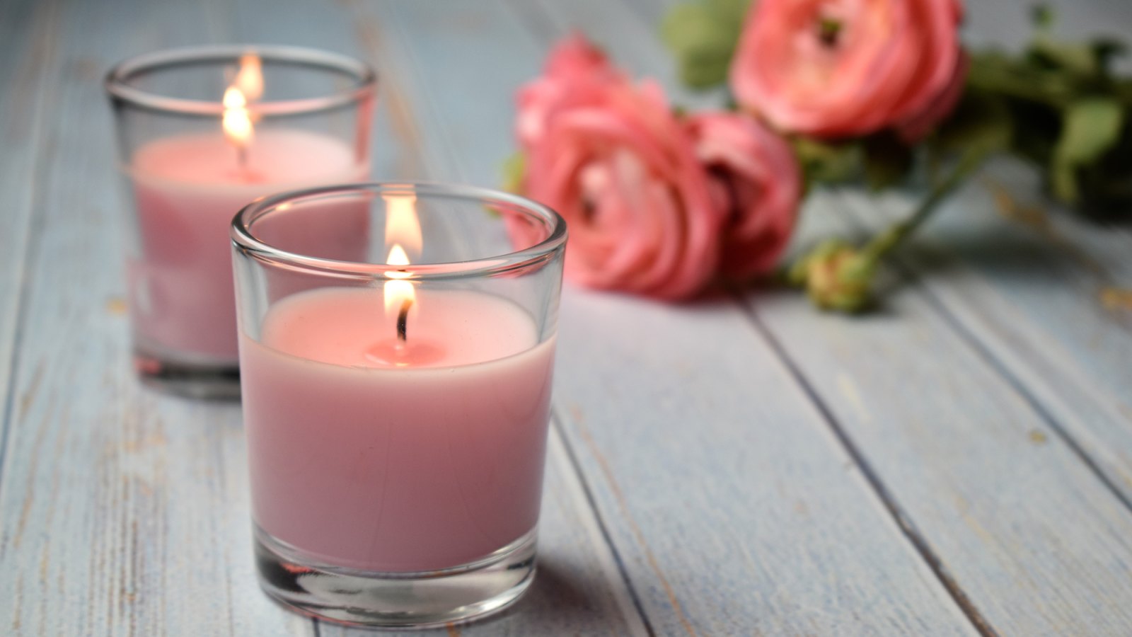 Scented pink candles with flowers in the background, close-up