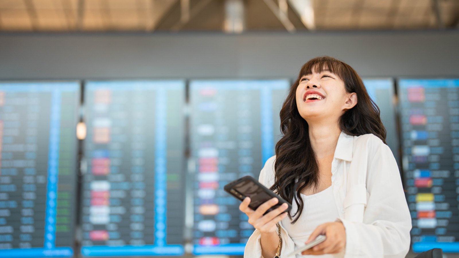 Smiling young woman text messaging on smartphone while waiting for her flight in airport lounge